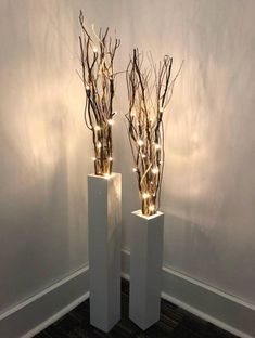 two white vases with branches and lights in them sitting on a carpeted floor