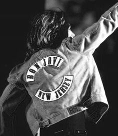 a woman wearing a pink jacket and jeans on stage with her arms in the air