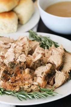 a white plate topped with sliced meat next to rolls and a cup of coffee on a table