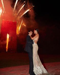 a man and woman standing next to each other in front of fireworks