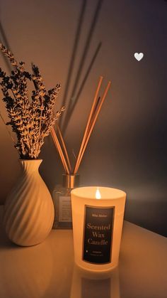 a lit candle next to a vase filled with flowers and reeds on a table