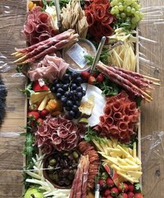 an assortment of meats, cheeses and fruit arranged on a platter with utensils