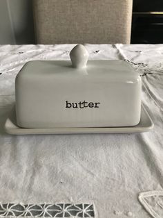 a white butter dish with the word butter on it sitting on a table next to a chair