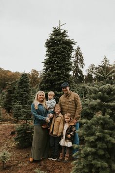 a family standing in front of a christmas tree at the holiday tree farm, surrounded by trees