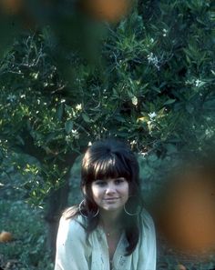 a woman sitting on the ground in front of a tree with leaves and branches around her