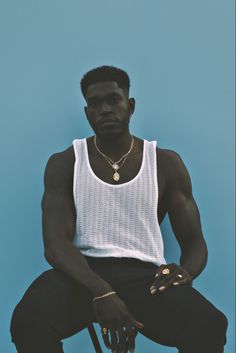 a man sitting on top of a chair wearing a white tank top and black pants