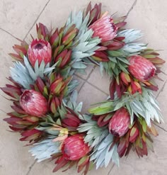 a wreath made out of red and green flowers on the ground next to a brick wall