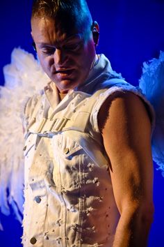 a man with white wings on his chest wearing a vest and looking at the camera