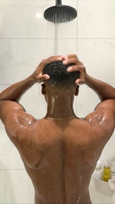 a man is taking a shower with his hands on his head and back to the camera