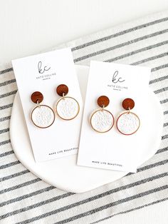 two pairs of earrings sitting on top of a white plate next to a black and white striped table cloth