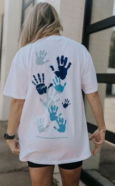 a woman walking down the street wearing a white shirt with blue hand prints on it