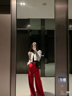 a woman taking a selfie in front of an elevator with red pants and white shirt