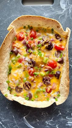 an open tortilla dish with tomatoes, olives and other vegetables in it