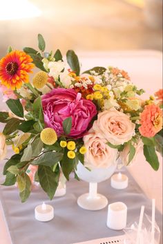 a vase filled with lots of flowers on top of a blue table cloth next to candles