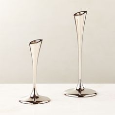 two tall silver vases sitting on top of a white counter next to each other