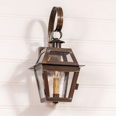 an old fashioned lantern hanging from the side of a wall with two candles in it