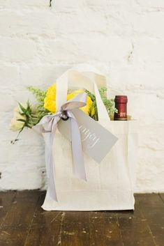 a tote bag with flowers and wine in it sitting on a wooden floor next to a white brick wall