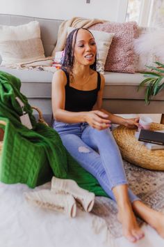 a woman sitting on the floor in front of a couch with pillows and blankets around her