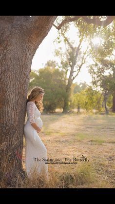 a pregnant woman standing next to a tree