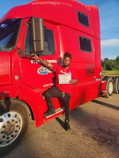 a man sitting on the side of a red semi - truck with his hand up