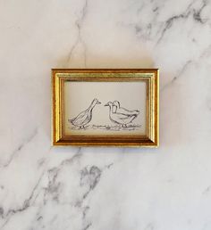 two birds kissing each other in a gold frame on a marble surface with white and black veining