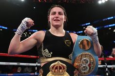 a woman standing in a boxing ring with her fists up and holding two different belts