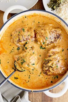 a pot filled with meat and gravy on top of a wooden table next to rice