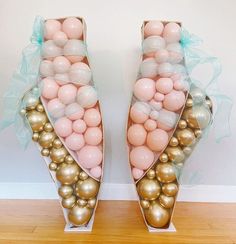 two vases filled with pink and gold balloons on top of a wooden floor next to a wall