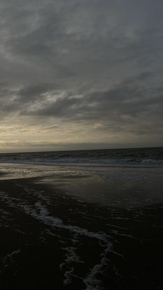 a person walking on the beach with a surfboard under an overcast cloudy sky