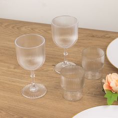 three clear glasses sitting on top of a wooden table next to a plate and flower