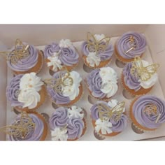 a box filled with cupcakes covered in purple frosting and gold butterfly decorations