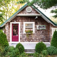 a small wooden house with a red door and window on the outside, surrounded by greenery