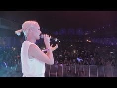 a woman standing in front of a crowd while holding a microphone to her mouth with both hands