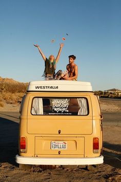 two people sitting on top of a van in the middle of the road with their arms up