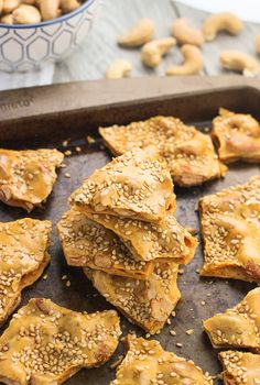 sesame seed crackers on a baking sheet next to a bowl of cashews