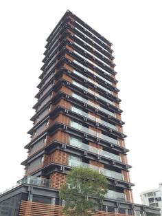 a tall building with lots of windows and balconies on the top floor, next to a tree