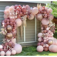 an arch made out of balloons and flowers on the grass in front of a house