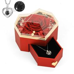 an open red box with a rose inside and two necklaces in the bottom, on a white background