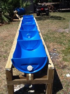 a long row of blue barrels sitting on top of a wooden pallet in the grass