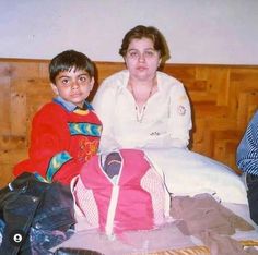 a woman sitting next to a young boy on a bed with clothes all over it