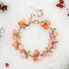 a bracelet with pink and orange beads on it in the snow next to pine cones