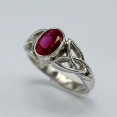 a silver ring with a red stone in the center and two intertwined bands around it