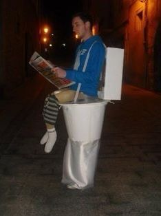 a man sitting on top of a toilet reading a newspaper