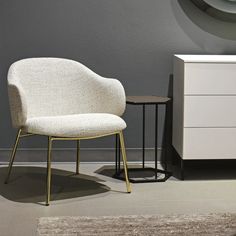 a white chair sitting next to a table with a clock on the wall behind it