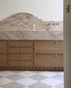 an empty bathroom with marble counter tops and drawers on the wall, in front of a checkered tile floor