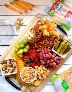 a wooden cutting board topped with fruit and snacks