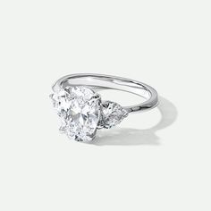 an oval diamond ring with three pear shaped diamonds on the side, set in 18k white gold