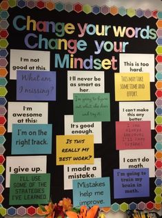 a bulletin board with words on it and flowers in vases sitting next to it