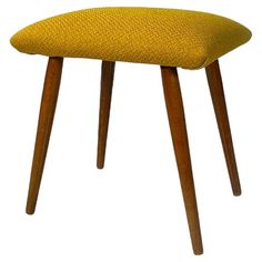 an upholstered stool with wooden legs and a yellow fabric seat cover on it