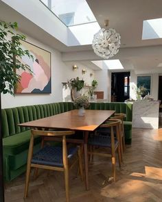 a dining room with green velvet couches and wooden table in the center, surrounded by potted plants